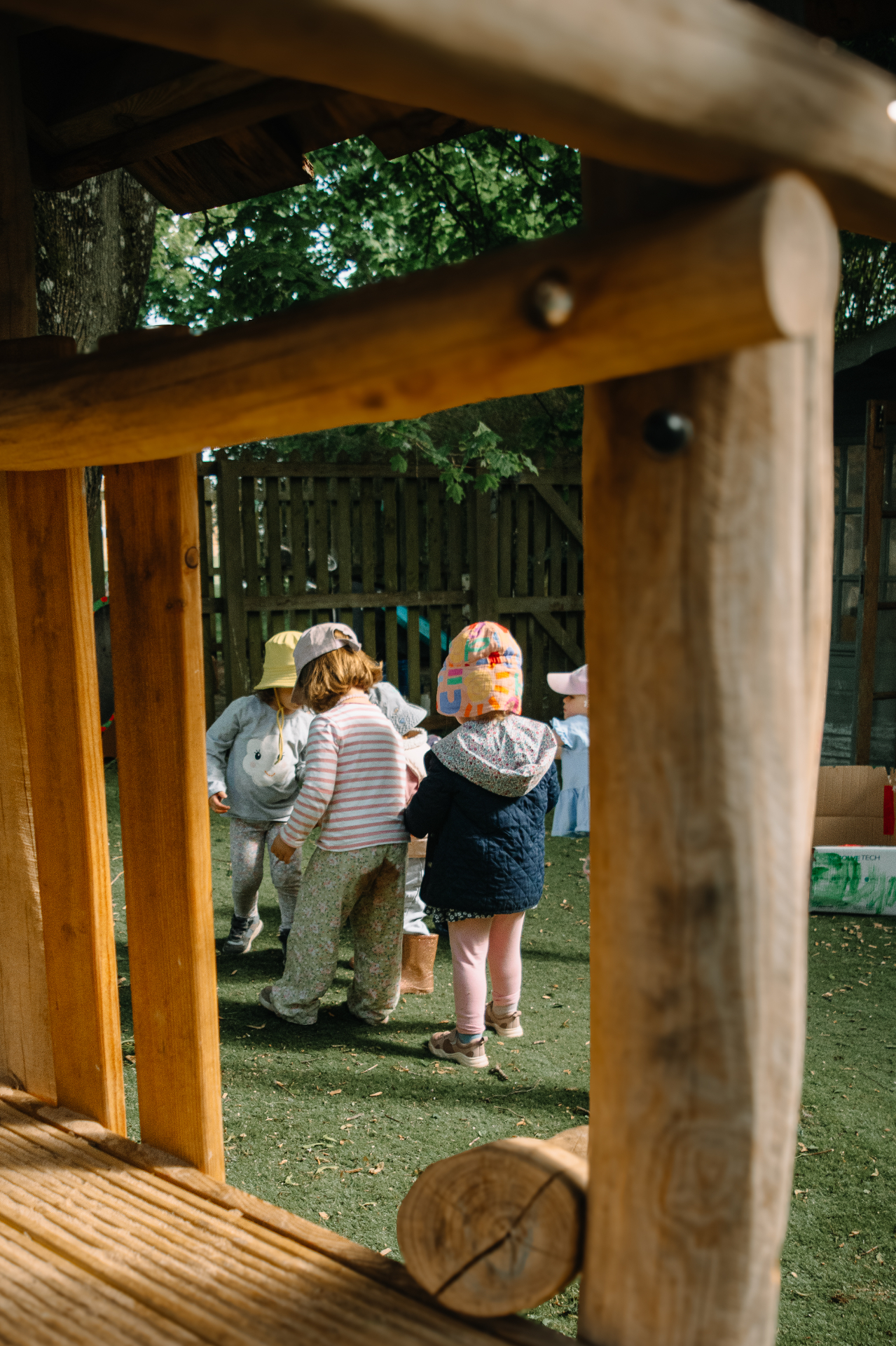 Children playing together in the nursery garden, seen through the wooden play frame