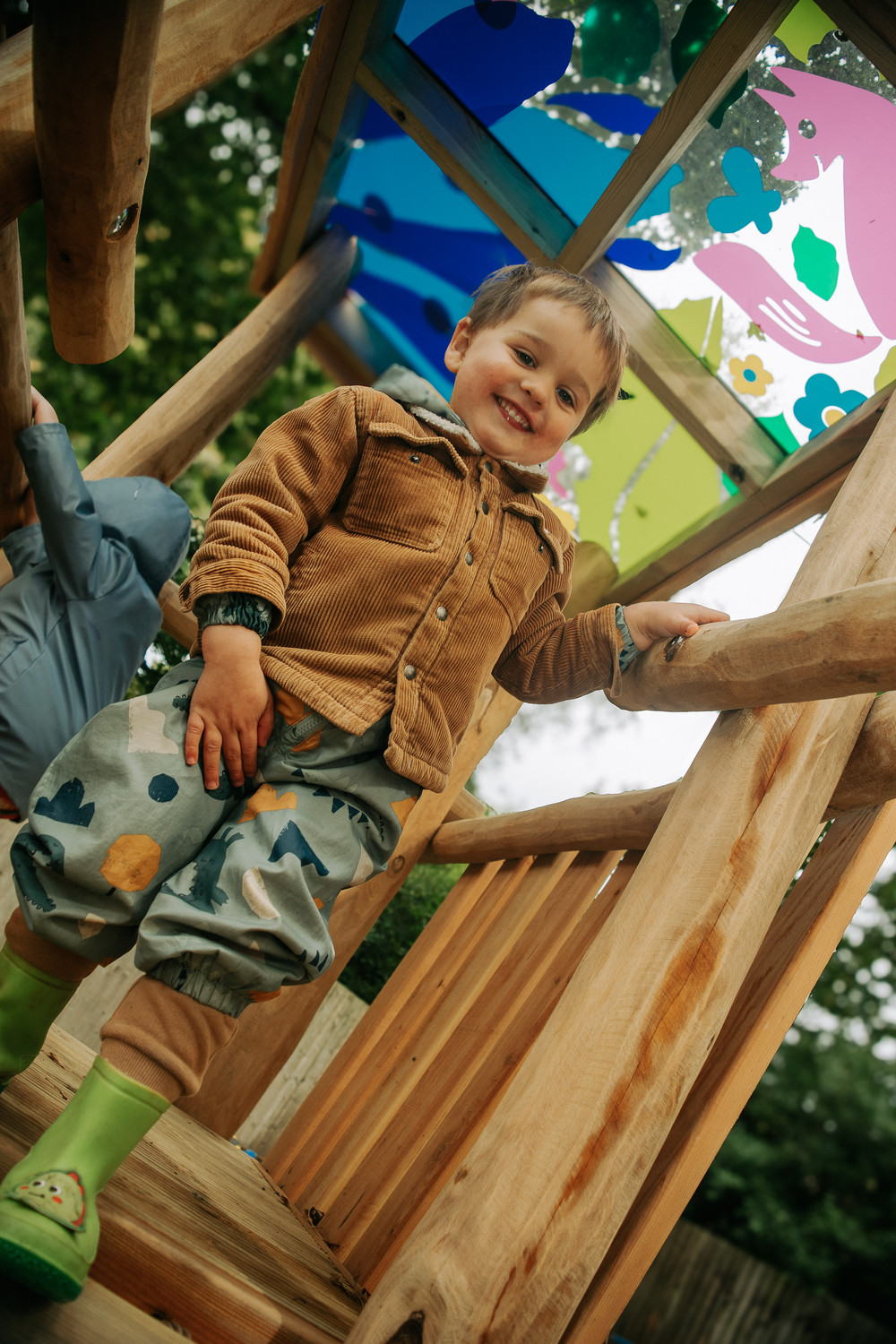 A child grinning at the top of the wooden climbing frame